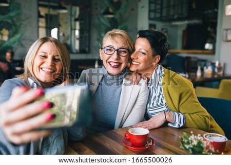 woman friends on coffee break at cafe, using smartphone for taking picture