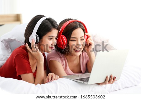 Happy Couple  asia woman wear headphones and enjoy musics playing mobile phone and tablet in bedroom.