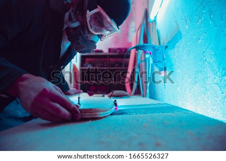 Skater in process of making his own skateboard, longboard - open business concept. Neon lighted studio of creating skateboards. Concept of openspace, craft production, workshop. Polishes, paints.