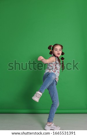 Cool young beautiful girl of eight years old in excellent mood with a funny hairstyle in a blue blouse with flowers indulges and grimaces on a bright green background
