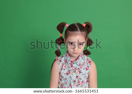 Cool young beautiful girl of eight years old in excellent mood with a funny hairstyle in a blue blouse with flowers indulges and grimaces on a bright green background