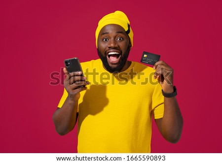Young man holds smart phone and credit card on red background