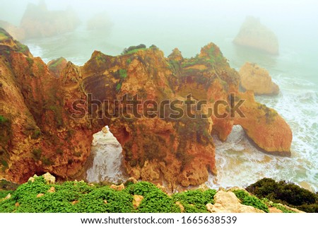 View of the characteristic rock formations near Três Irmãos beach on a day of thick fog in Alvor on the Algarve coast of Portugal