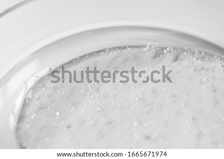 Close-up transparent gel cleanser with air bubbles in glass petri dish on white background with selective focus.  Cosmetic texture