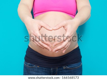 Close up portrait of a pregnant young woman showing heart shape with hands in front of stomach