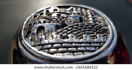 Relief image of the city on a silver pen stand (side face, closeup, angle).
