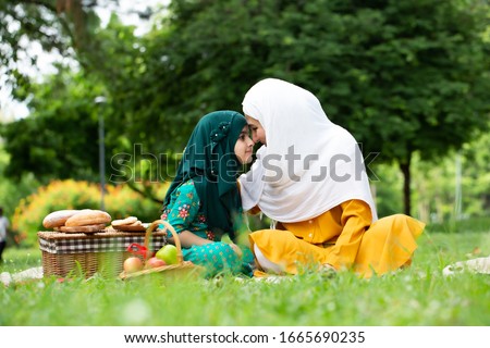 Happy Muslim family mom and child concept. Young Asian Muslim Mother and her daughter child girl with hijab dress smiling,hugging and kissing together.Happy mother and daughter at picnic outdoors.