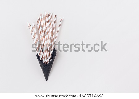 Cocktail straws with golden stripes in black ice-cream horn on pastel beige background with copy space. Creative and moody picture. Top view.