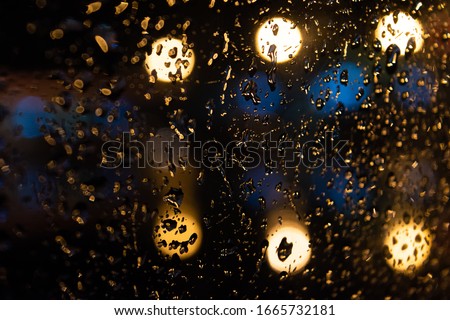 rain drops on the glass at night with colorful light bokeh. Abstract dark and blured background