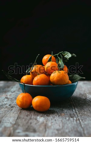 Stock Photography of blue bowl with set of tangerines or oranges, on a wooden table with black background