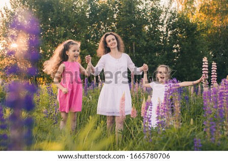 Mom and two daughters in dresses in a field with flowers