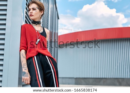 Young stylish woman standing leaning on wall outdoors urban background looking aside pensive