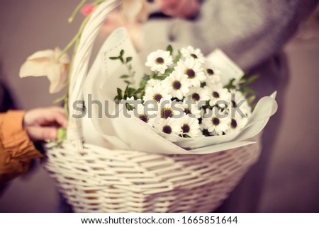 
White chrysanthemums in a white basket carries a beautiful girl and a little boy touches flowers with his hands.