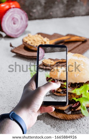 hands picking up a smartphone taking a picture of a burger. Space for text. Selective focus