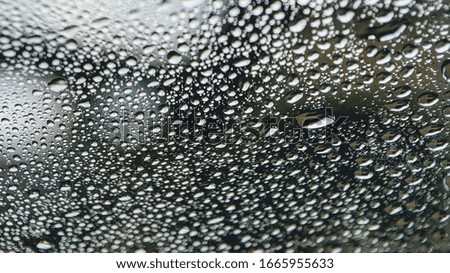 Raindrops on a car glass or windshield, rural life in the rainy season abstract background. Selective focus.
