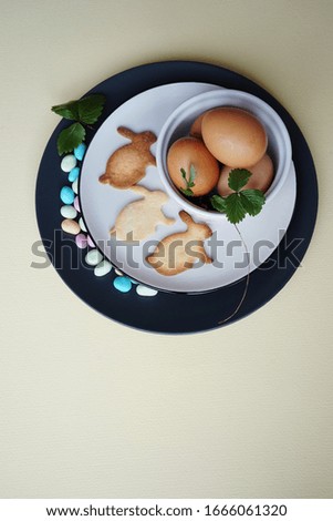  Happy  Easter eggs with green leaves of strawberries, bunny-shaped cookies and colored sweets on a light background. Copy space                