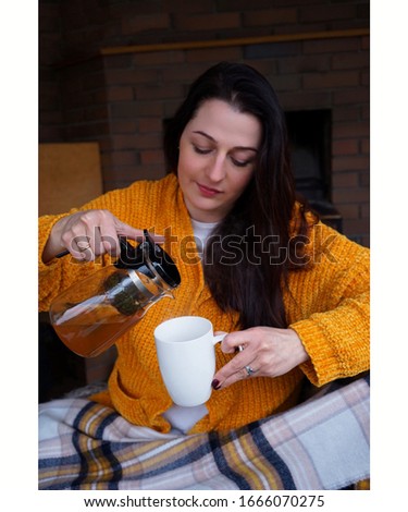 
a girl in a yellow sweater pours tea from a teapot into a white cup