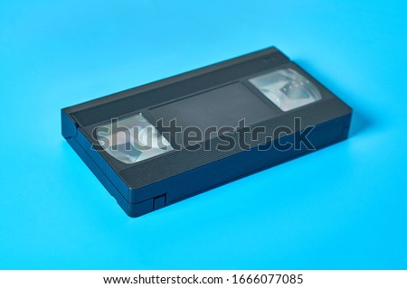 Single black old plastic vhs video cassette lies on blue desk. Concept of 90s. Close-up