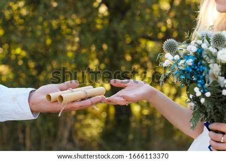 Wedding vowes on rolled paper sheet on groom palm, wedding bouquet, rustic outdoor wedding concept.