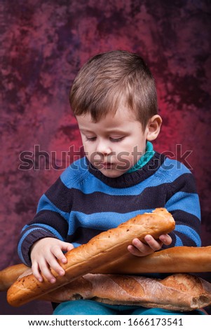 Cute kid holding French bread against dark red background. Little boy eating the french baguette