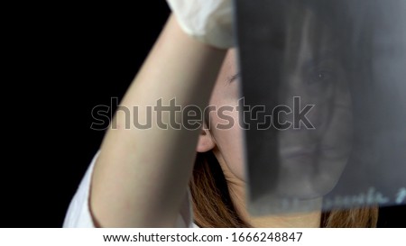 Young woman doctor checks the results of an x-ray of the foot. A girl is considering a close-up x-ray. On a black background. View through an x-ray image.