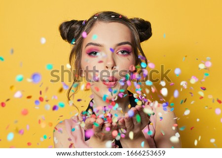 Beautiful model woman and falling colorful confetti on yellow background