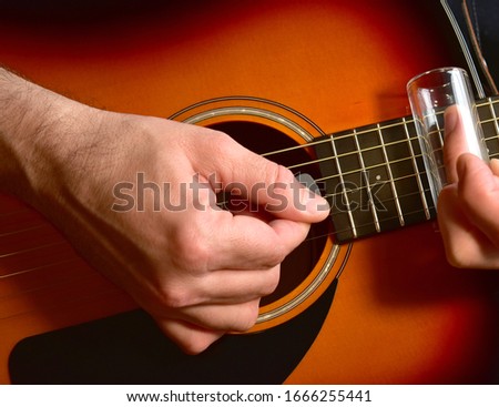 Man playing an acoustic guitar with a glass slide. 