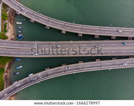 Aerial top down view of the beginnig of the bridge with the shore, fishing boat and greenish colour sea water background. 