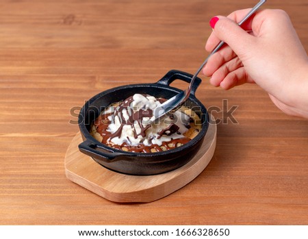 Vanilla ice cream with chocolate syrup and cookie base being enjoyed. Hand holding spoon taking ice cream. wooden background