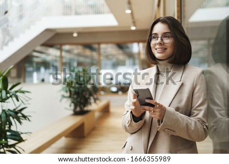 Portrait of successful happy smiling woman just finished meeting with business partners, signed deal company, holding mobile phone and look away with dreamy pleased expression