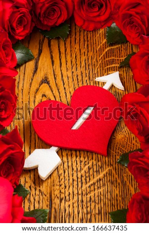 heart pierced by  cupid arrow and red roses on the wooden background