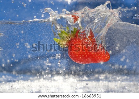 A juicy red strawberry plunging into some water.