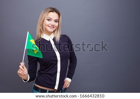 Immigration and the study of foreign languages, concept. A young smiling woman with a Brazil flag in her hand. Girl waving a Brazilian flag on a gray background
