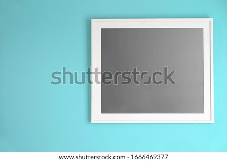 White empty photo frame hanging on turquoise color wall