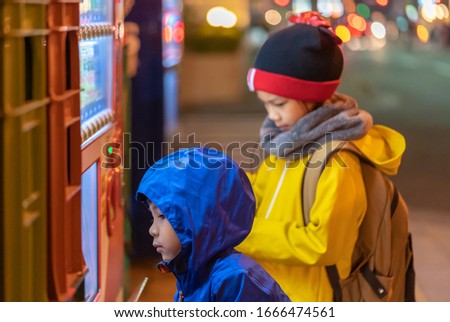 Two children is choosing drinks from Japanese Vending machine near Sendai station at night.