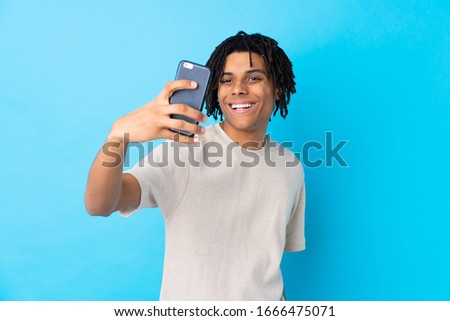 Young African American man over isolated blue background making a selfie