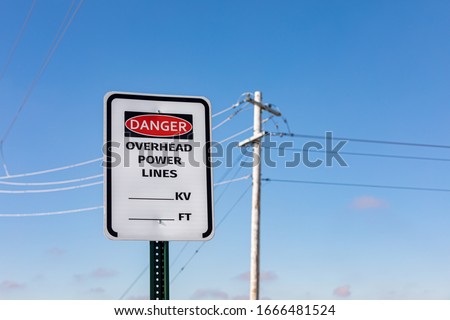 Road sign warning of overhead power lines danger. Electrical transmission wires and pole in background