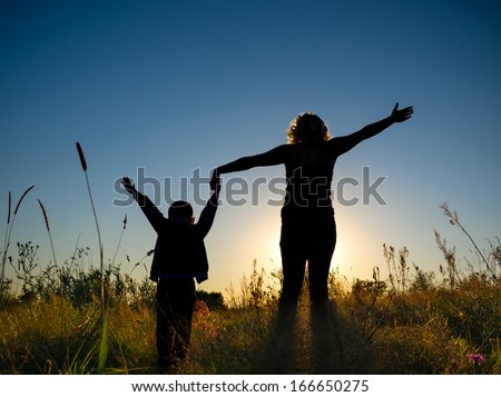 Silhouette of a young boy and his mother in the field in summer 