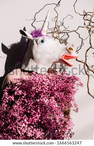 Weird woman wearing a unicorn rubber mask holding big and beautiful bunch of fresh baby breath flowers in pink colors, cropped photo, bouquet close up