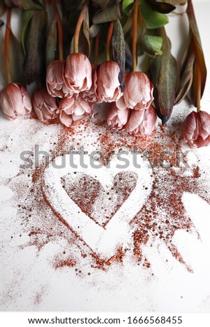 Brown pink tulips on white background next to a heart made of glitter