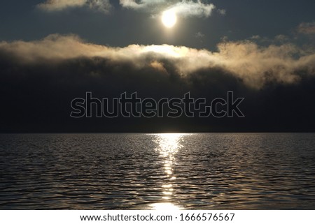 View of morning fog rising over water and lit by the sun creating a misterious dramatic picture.