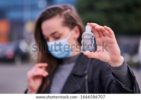Woman in medical protective mask with an antibacterial antiseptic gel for hands disinfection outdoors. Health protection prevention during flu virus outbreak and coronavirus epidemic Royalty-Free Stock Photo #1666586707