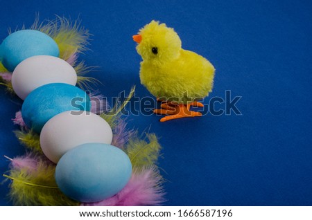 Toy chicken with white and blue Easter eggs with feathers on a classic blue background with copy space. Side view. Happy easter.