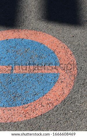 Close up view of a circular traffic sign painted on a grey asphalt road. Circular symbol forbidding cars to park at the place. Abstract design of a textured surface with red, blue and grey colors. 