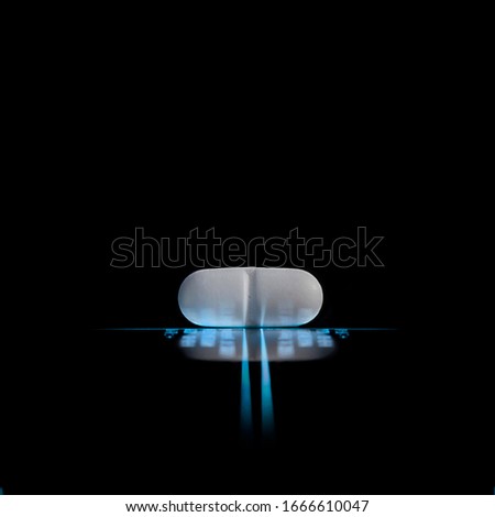 one white pill lying in the luminous light lines with blurred figures and letters with reflection isolated on black background