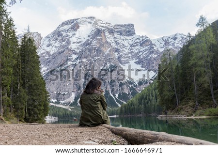 brunette woman poses on her back at Lago di Braies, impressive green lake, which reflects the high snowy mountains, surrounded by abundant green vegetation