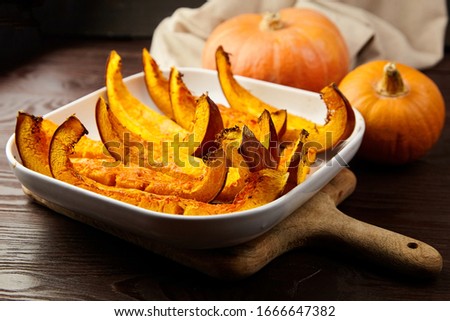 Slices of baked pumpkin in white ceramic bowl on brown wooden table, closeup, selective focus. Vegetable dish, vegan diet, healthy food