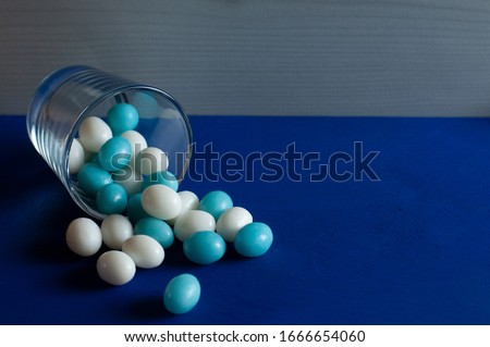 easter eggs of sugar in blue and white color pouring out of a glass to blue painted wooden board