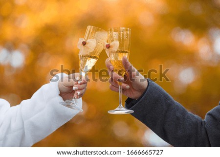 two decorated  glasses with champagne  in the hands of bride and groom.
place of celebration wedding outdoors. couple with decorated wine glasses on  wedding day close up. romantic date