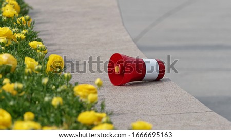 Red and white loudspeaker placed on flower bed in public place to remind everyone to wear masks.